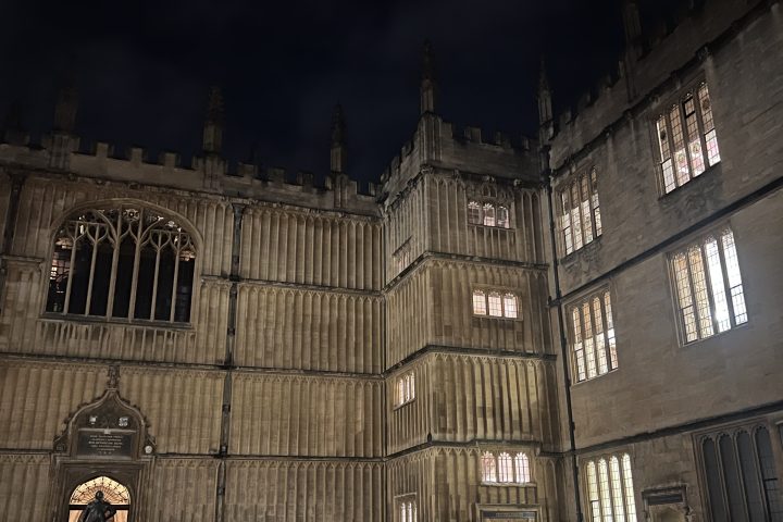Historic building at night with illuminated windows and wet pavement.