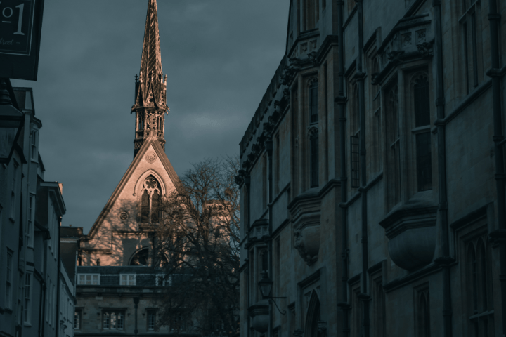 Tall church spire with intricate architecture, seen between shadowed narrow buildings.