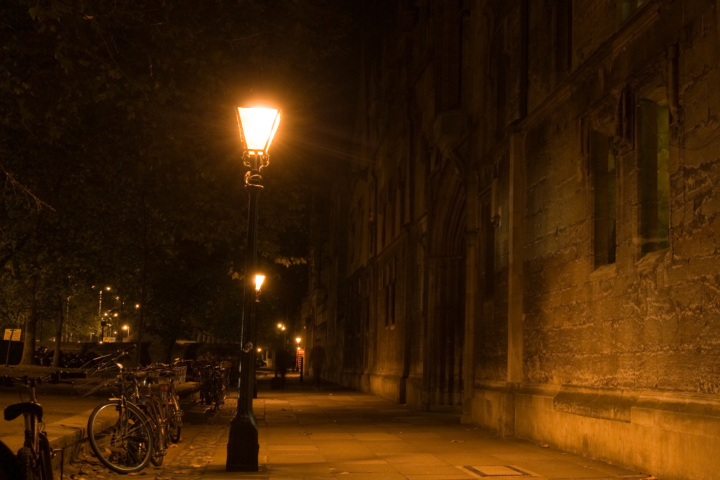 Dimly lit cobblestone street with bicycles and glowing lampposts at night.