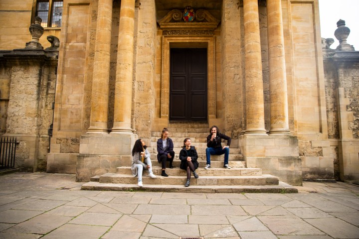 Four people sitting on stone steps outside a historic building with columns.