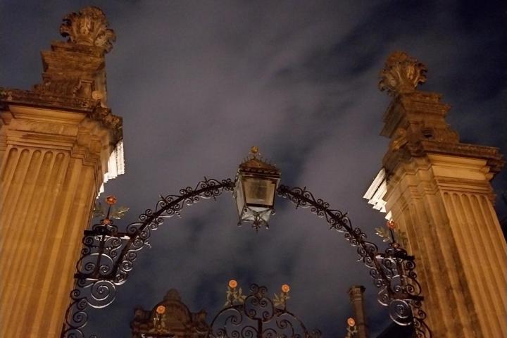 Ornate gated entrance with stone pillars under cloudy night sky.