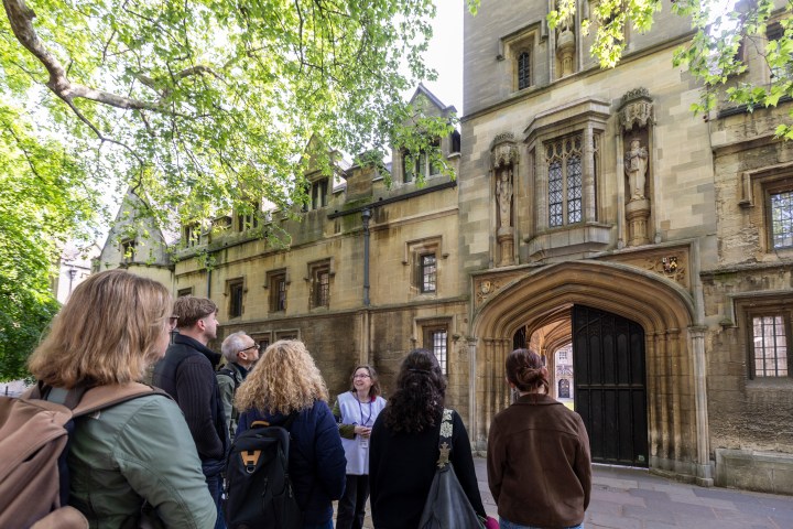 People stand outside an old stone building with arched windows and a wooden door.