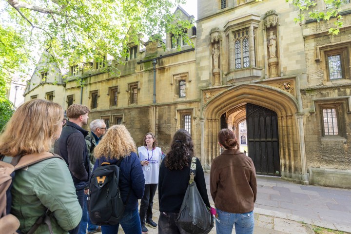 Tour guide leads a group by a historic stone building with arched entrance.