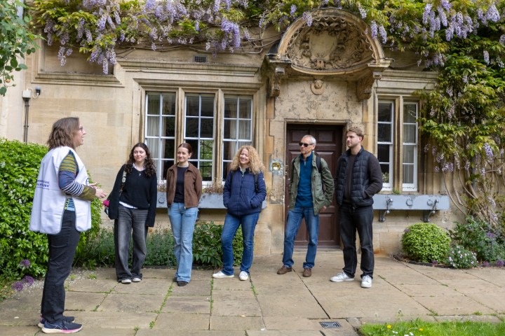 Group of people on a guided outdoor tour beside a historic building with wisteria.