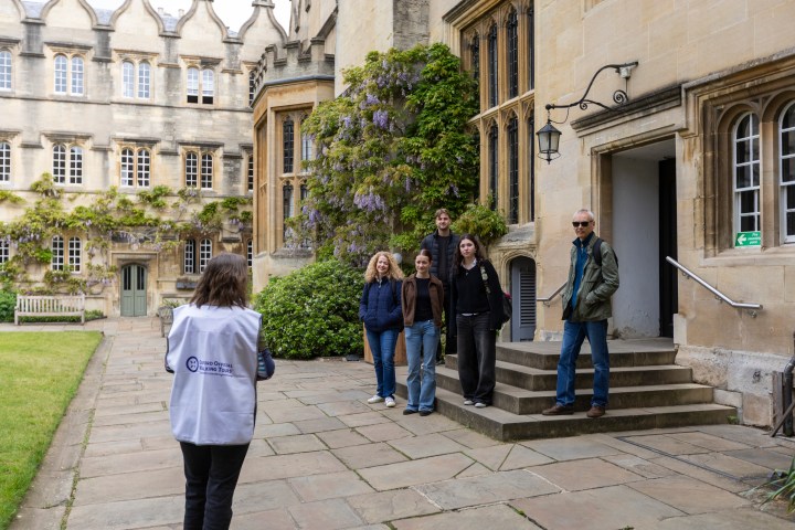 Five people pose on steps outside a historic building while a person photographs them.