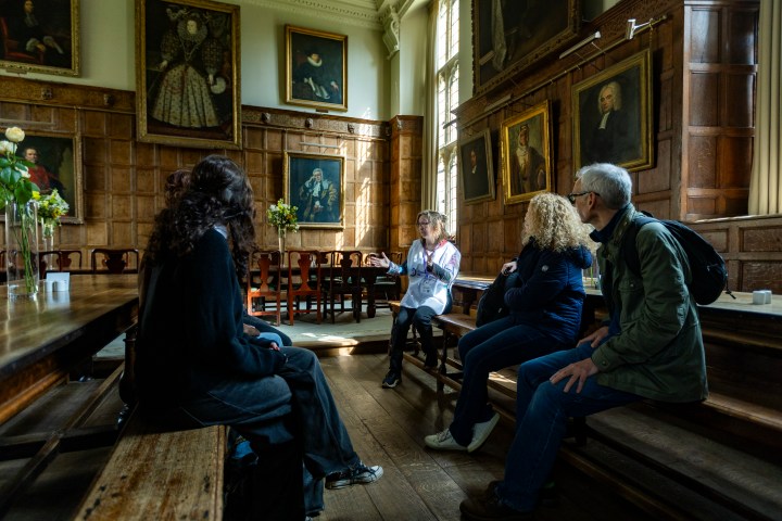 Group sitting in historic room with wooden panels and portraits.