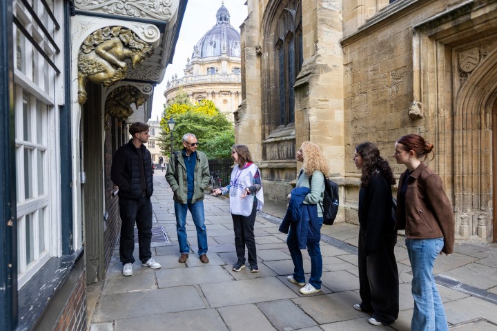 Group of people talking near historic building with domed structure in background.