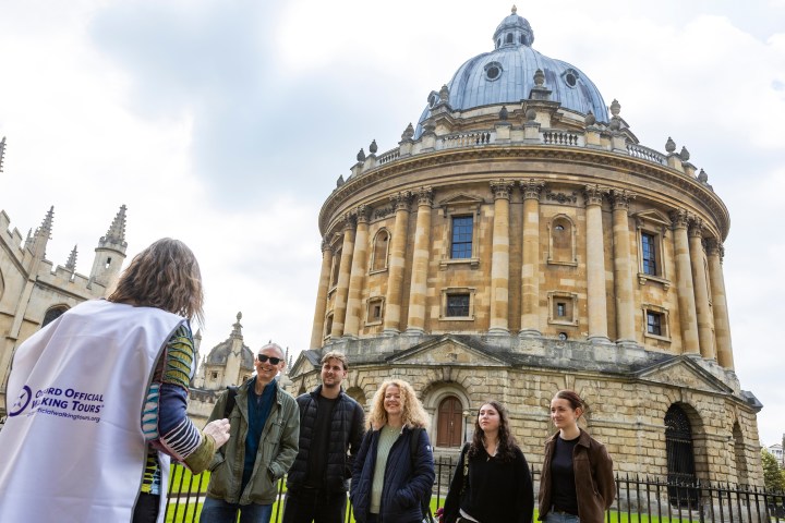 Tour group in front of historic, domed building with guide wearing a vest.