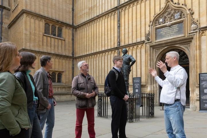 Guide speaks to group outside historic building with a statue.