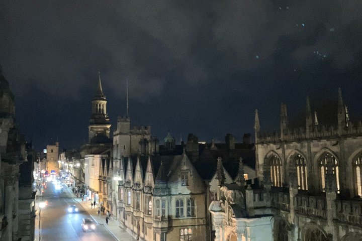 Historic city street at night with illuminated buildings and a tall spire.