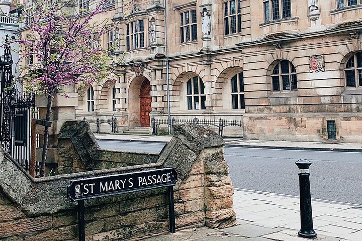 Stone building with sign 'St Mary's Passage' and blooming tree.