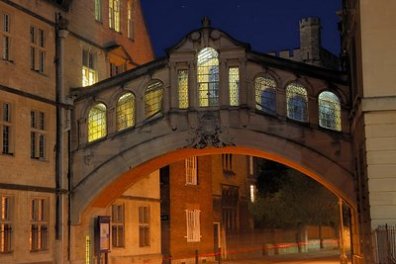 Illuminated arched bridge connecting buildings at night.