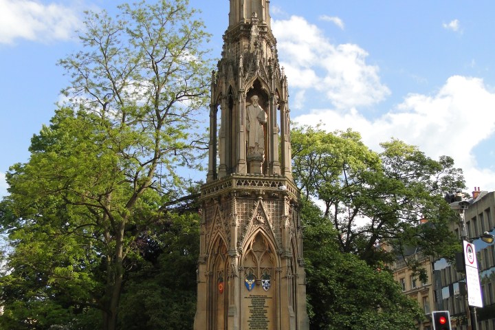 a large tall tower with a clock on the side of a road