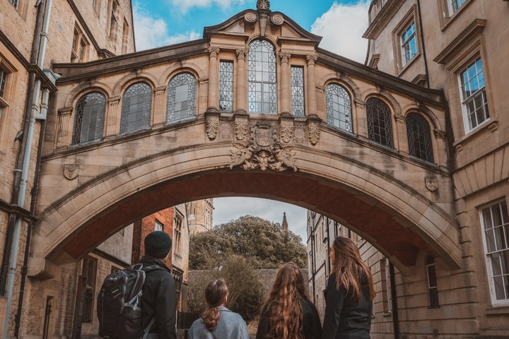 Four people stand under a stone arch bridge with ornate windows.