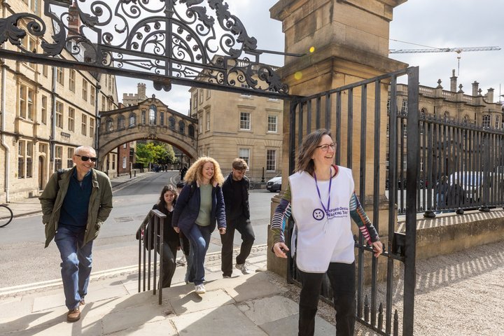 People walking through an ornate gate on a sunny day, led by a person in a volunteer vest.