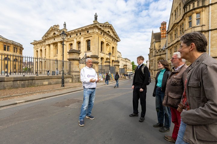 Tour guide speaking to a group outside historic buildings on a sunny day.
