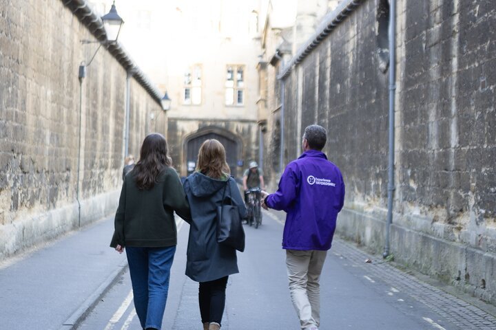 Three people walk down a narrow, historic stone alleyway.