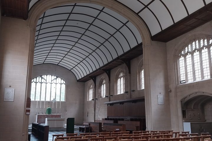 Interior of a church with wooden chairs and large arched windows.