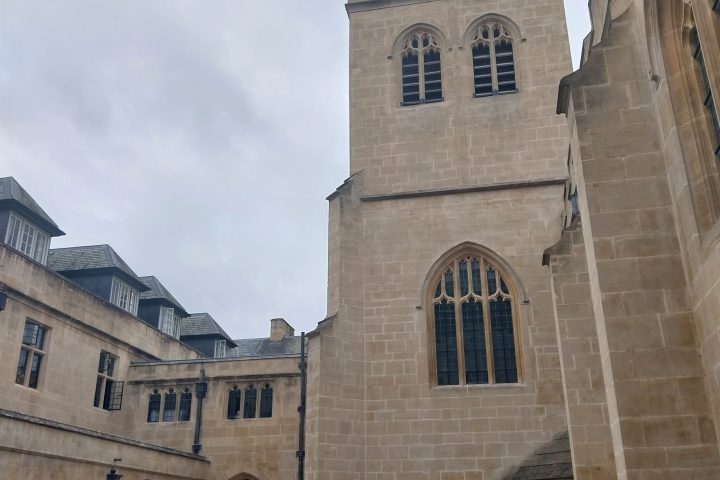 Historic stone building with tower and arched windows on a cloudy day.