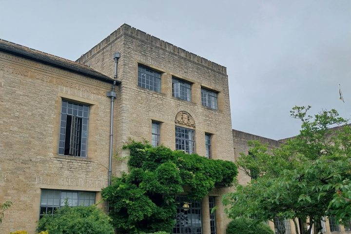 Brick building with windows, greenery, and cloudy sky.