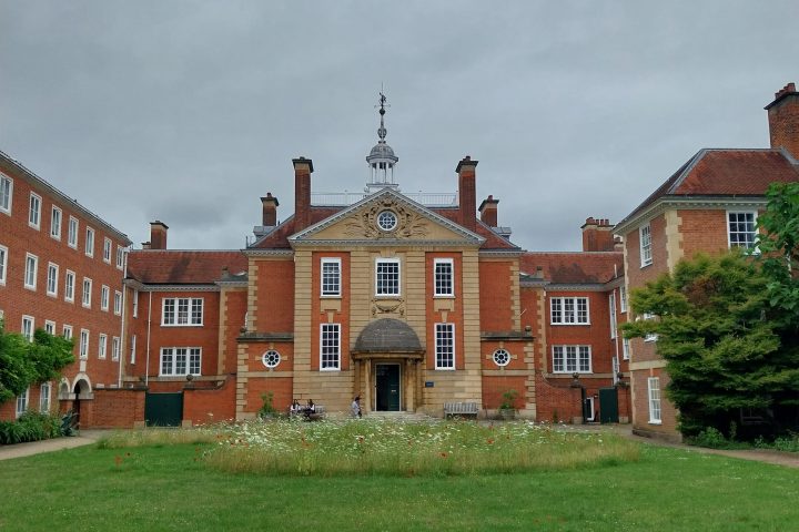 Historic brick building with clock tower and green lawn on a cloudy day.