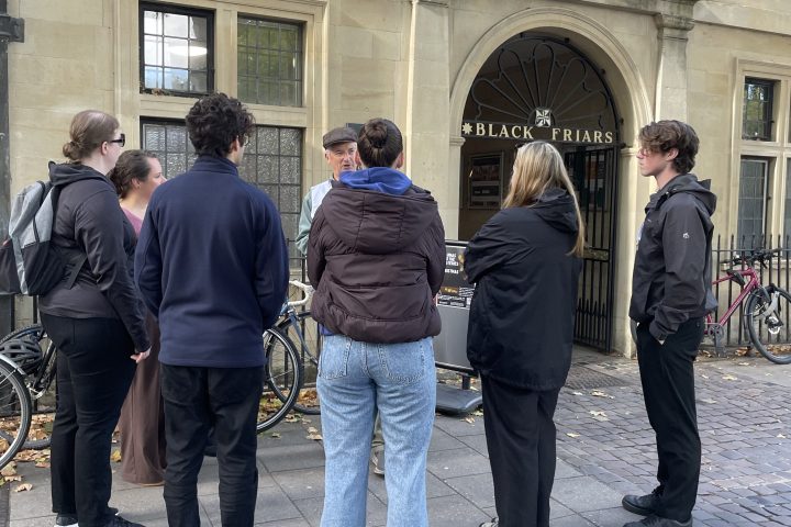 Group of people standing on a sidewalk near a historic building entrance.
