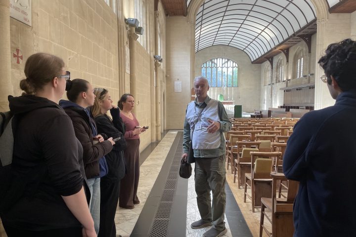 Man standing, engaging with seated group in a bright hall.