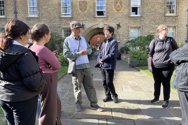 Group of people standing outside a stone building on a sunny day.