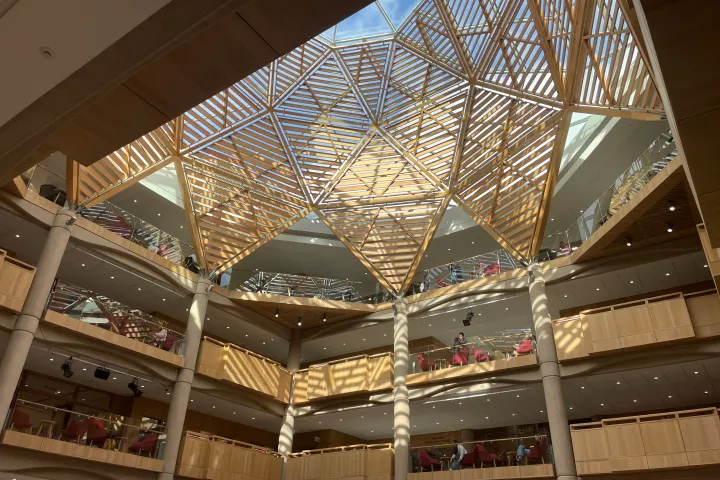 Modern atrium with geometric wood ceiling and multiple floors.
