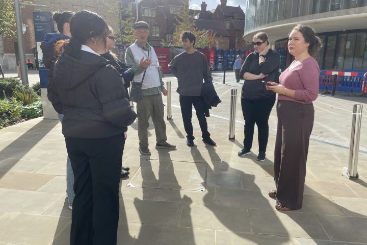 People standing and talking outside on a sunny day in formal attire.