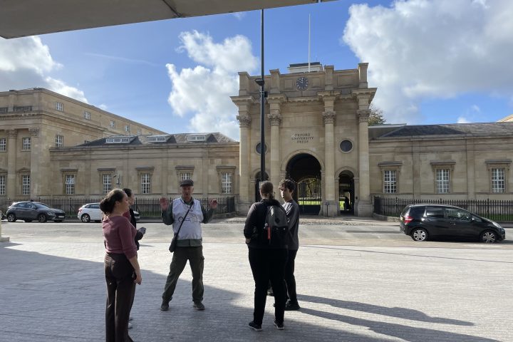 People standing near a historic building with a clock tower on a sunny day.