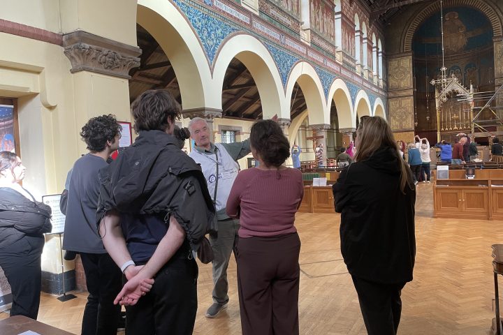 People in a historic building with arched ceiling and intricate wall designs.