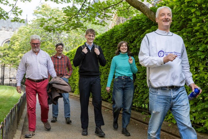 Five people walking outdoors on a path surrounded by greenery.