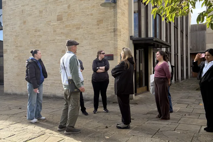 Group of people standing and talking outside a building on a sunny day.