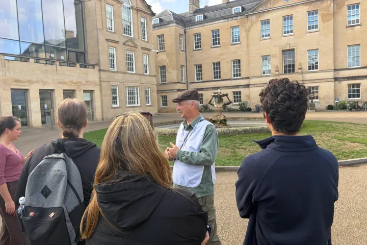 Guide speaks to tourists near a historic building and fountain.
