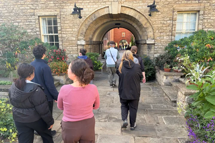 Group walking through stone archway in courtyard with plants.